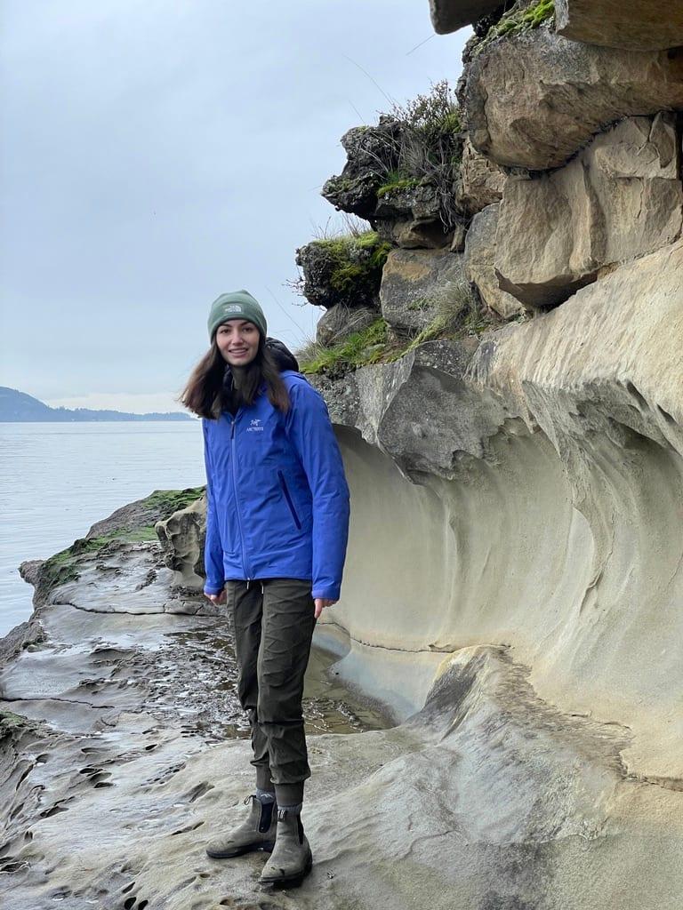 Madison Ordway, Founder and CEO of Real Health Diagnostics, standing on a coastal sandstone shelf above the water on an overcast day