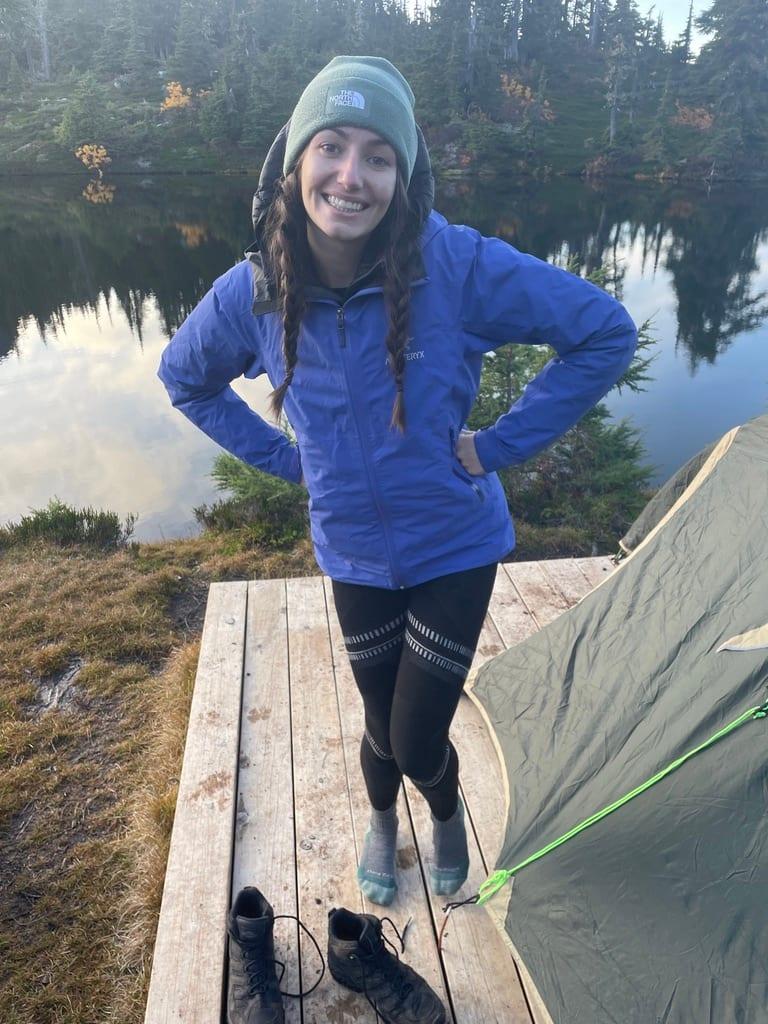 Madison at a backcountry campsite, standing on a wooden tent platform beside a calm alpine lake