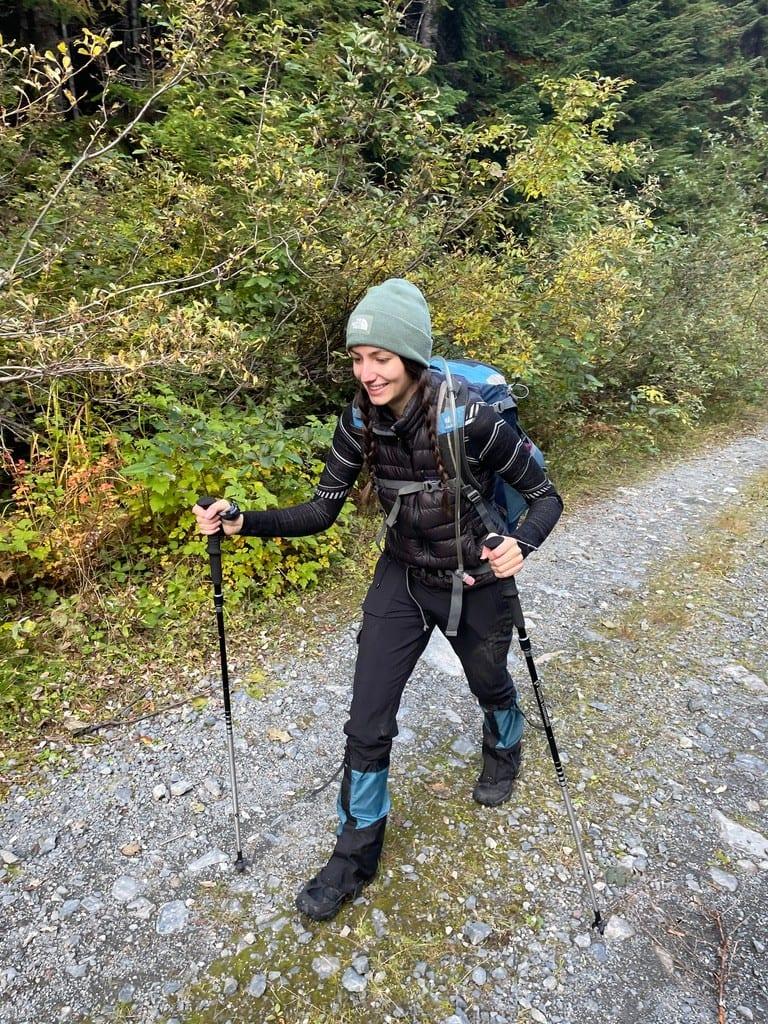 Madison hiking a forested gravel trail with trekking poles and a backpack